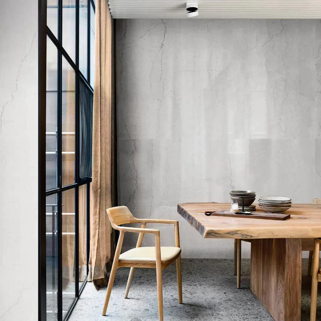Comedor moderno con pared y piso de porcelanato gris, mesa de madera y ventanal grande.