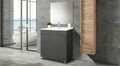 Mueble para baño gris con lavabo blanco, monomando y espejo, sobre piso y pared de concreto.