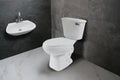 Sanitario y lavabo blanco modernos para baño, sobre pared de azulejo gris y piso blanco.